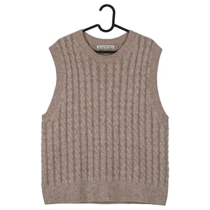 May include: A tan cable-knit sweater vest with a crew neck, hanging on a black hanger. The vest has a textured pattern and the brand name "Acne Studios" is visible on the neckline.