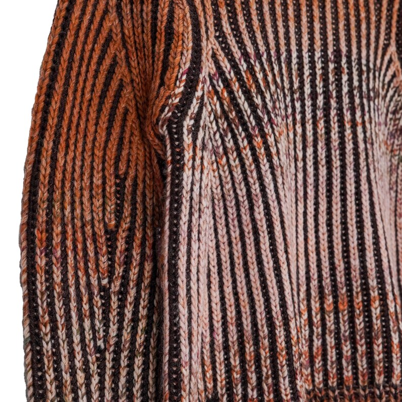 May include: Close-up of a knitted sweater with vertical stripes in shades of brown, orange, and cream. The knitwear features a textured pattern and a subtle color gradient, creating a warm and inviting aesthetic.