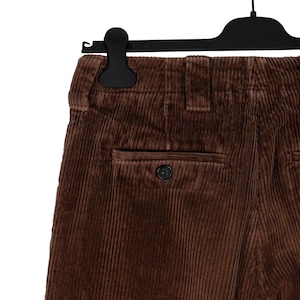 May include: Close-up of brown corduroy pants hanging on a black hanger. The pants have a single back pocket with a button closure. The corduroy fabric has vertical ridges.