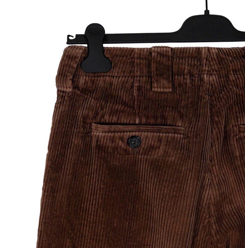May include: Close-up of brown corduroy pants hanging on a black hanger. The pants have a single back pocket with a button closure. The corduroy fabric has vertical ridges.