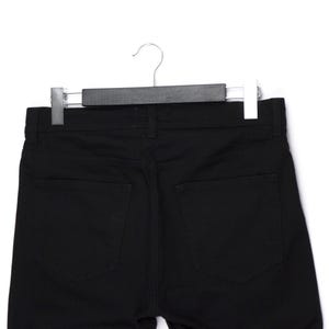 May include: A pair of black denim pants hanging on a black hanger. The pants have two back pockets and a classic five-pocket design. The fabric appears to be a medium-weight denim.