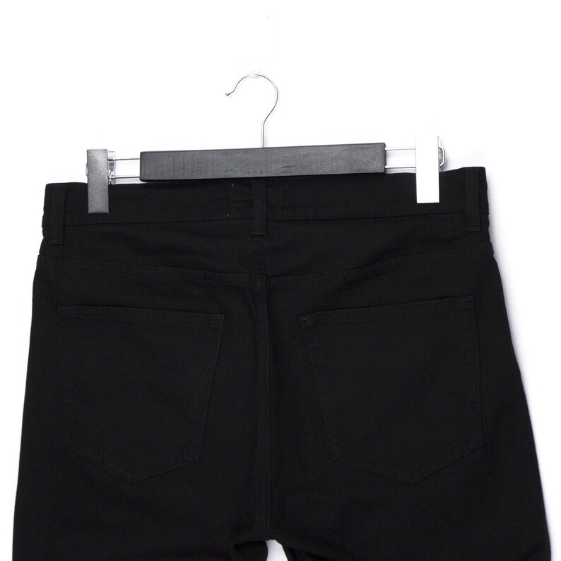 May include: A pair of black denim pants hanging on a black hanger. The pants have two back pockets and a classic five-pocket design. The fabric appears to be a medium-weight denim.
