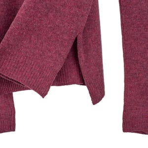 May include: Close-up of a burgundy-coloured sweater. The knitwear features a split hem design and ribbed cuffs. The fabric has a textured appearance, suggesting a warm and comfortable material. The sweater is a solid colour, suitable for various outfits.
