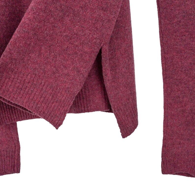 May include: Close-up of a burgundy-coloured sweater. The knitwear features a split hem design and ribbed cuffs. The fabric has a textured appearance, suggesting a warm and comfortable material. The sweater is a solid colour, suitable for various outfits.