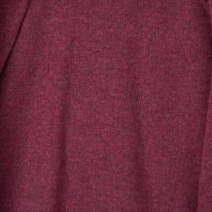 May include: Close-up of a burgundy-coloured knit fabric. The material has a textured appearance with subtle colour variations, creating a heathered effect. The fabric appears soft and likely suitable for clothing.