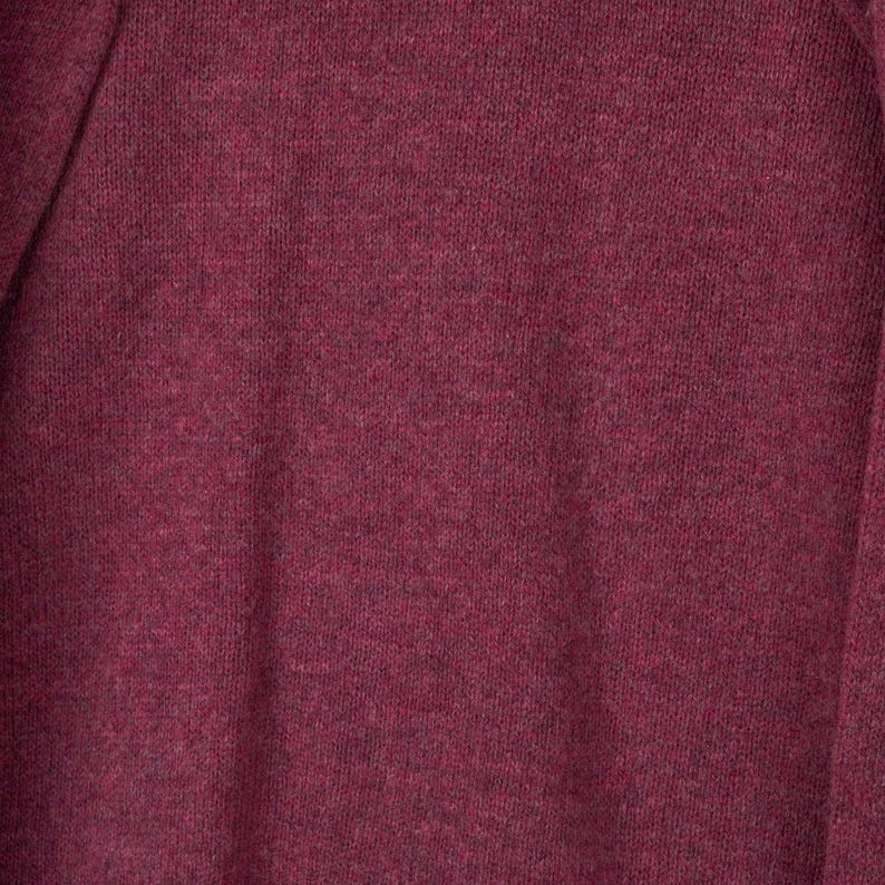 May include: Close-up of a burgundy-coloured knit fabric. The material has a textured appearance with subtle colour variations, creating a heathered effect. The fabric appears soft and likely suitable for clothing.