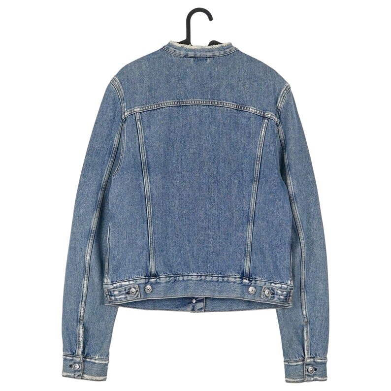 Op de afbeelding: Een lichtblauwe spijkerjas, van achteren gezien, hangend aan een zwarte hanger. De jas heeft een klassiek ontwerp met een kraagloze halslijn, knoopsluitingen en twee borstzakken. De denim heeft een verweerde uitstraling.