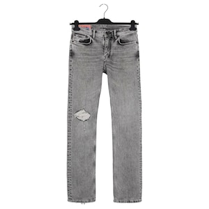 Puede incluir: Vaqueros grises con un detalle de rodilla desgastada, colgados de una percha negra. Los vaqueros tienen un diseño clásico de cinco bolsillos y un corte recto. El lavado es gris descolorido, dándoles un aspecto desgastado.