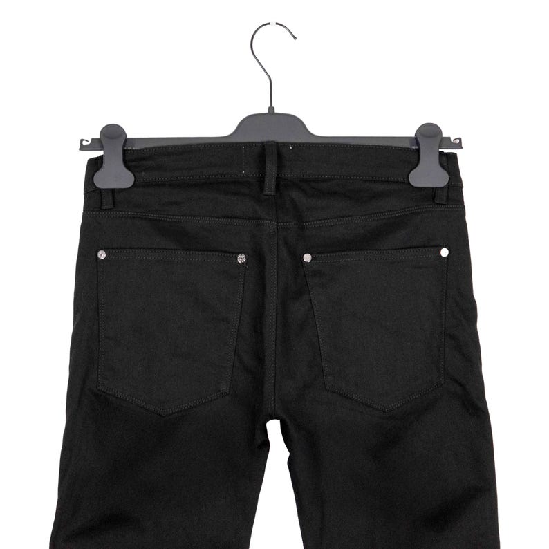 May include: Black denim jeans hanging on a black hanger. The jeans have two back pockets with silver-colored embellishments. The jeans are a solid black color.