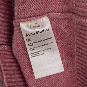 May include: Close-up of a pink knit sweater with a tag from Acne Studios. The tag reads "XS" and "175/88A". The tag also includes the text "MADE IN CHINA" and "100% WOOL".