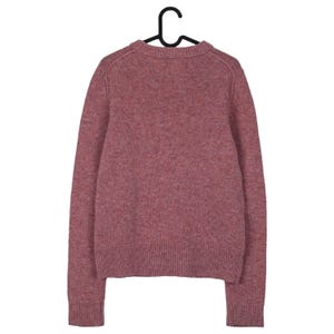 May include: A dusty rose-colored sweater with long sleeves hangs from a black hanger. The knitwear has a crew neck and ribbed cuffs and hem. The sweater's texture appears soft and warm, suitable for cooler weather. The garment is displayed against a plain white background.