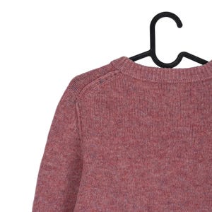 May include: A dusty rose-colored sweater with a crew neck, hanging on a black hanger. The knitwear has a textured appearance, with visible stitching details on the shoulder seams. The sweater's color is a muted, reddish-pink.