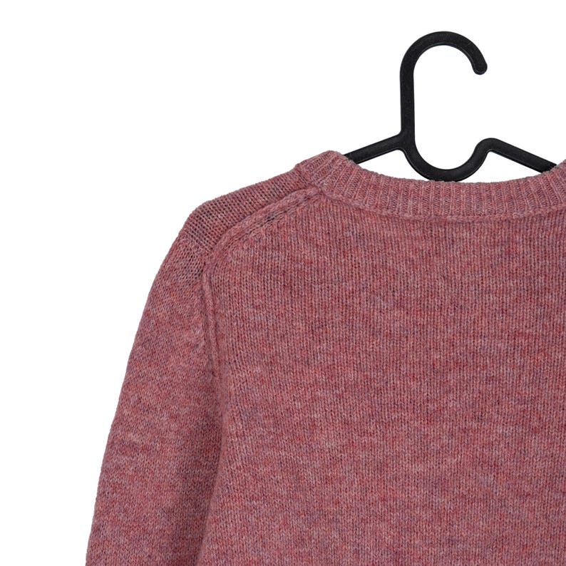 May include: A dusty rose-colored sweater with a crew neck, hanging on a black hanger. The knitwear has a textured appearance, with visible stitching details on the shoulder seams. The sweater's color is a muted, reddish-pink.