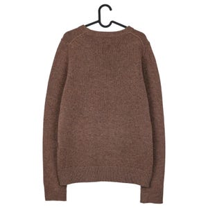 May include: A brown sweater with a crew neck, hanging on a black hanger. The sweater has long sleeves and a ribbed hem and cuffs. The knitwear is a solid color, with a textured appearance.
