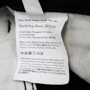 May include: A white clothing label with black text, featuring the text "North Stay Black, 30/176-141". The label includes the Acne Studios logo, fabric composition details, and washing instructions. Made in Italy.