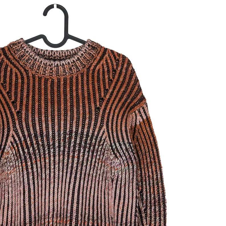 May include: A striped sweater in shades of brown, black, and pink hangs on a black hanger. The sweater features a ribbed knit design with vertical stripes. The neckline and shoulders are visible, showcasing the garment's texture and pattern.