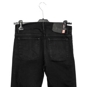 May include: Black denim jeans hanging on a black hanger. The jeans feature two back pockets and a leather patch. The denim is a solid black colour.