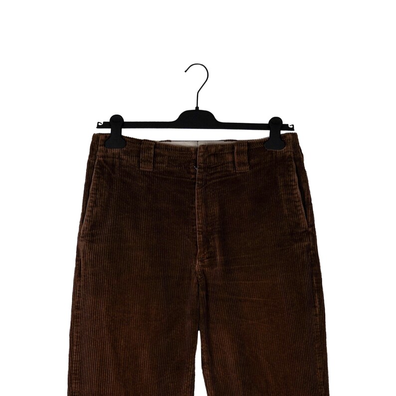 May include: Brown corduroy pants hanging on a black hanger. The pants have a classic five-pocket design and a straight leg. The corduroy fabric has a ribbed texture and a rich, warm brown color.