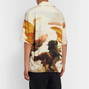 May include: Short-sleeved button-up shirt with a landscape and horse painting design. The shirt features a cream-colored base with a colorful print of horses and a mountainous landscape.