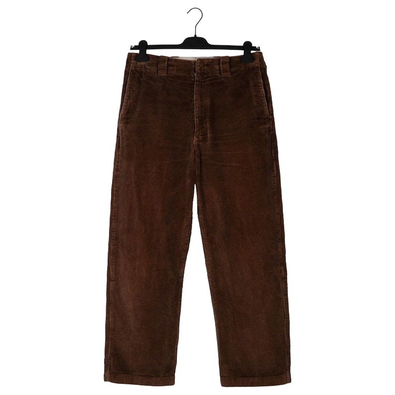 May include: Brown corduroy pants hanging on a black hanger. The pants have a classic, straight-leg design with a button and zipper closure. The corduroy fabric has a ribbed texture and a rich, warm brown color.