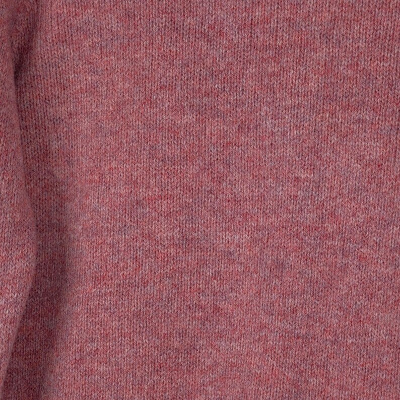 May include: Close-up of a knitted sweater in a dusty rose color. The fabric has a textured appearance with a subtle heathered effect, showcasing a blend of pink and purple threads. The knitwear appears soft and warm.