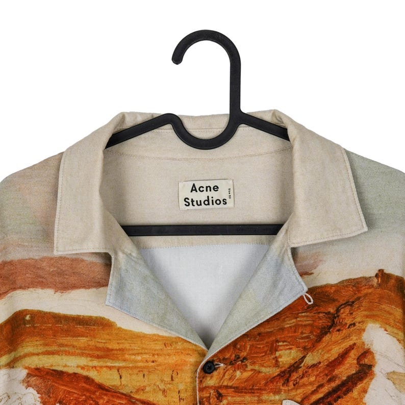 May include: A button-down shirt with a landscape design in shades of orange, brown, and blue. The shirt has a beige collar and the "Acne Studios" label is visible. The shirt is hanging on a black hanger.