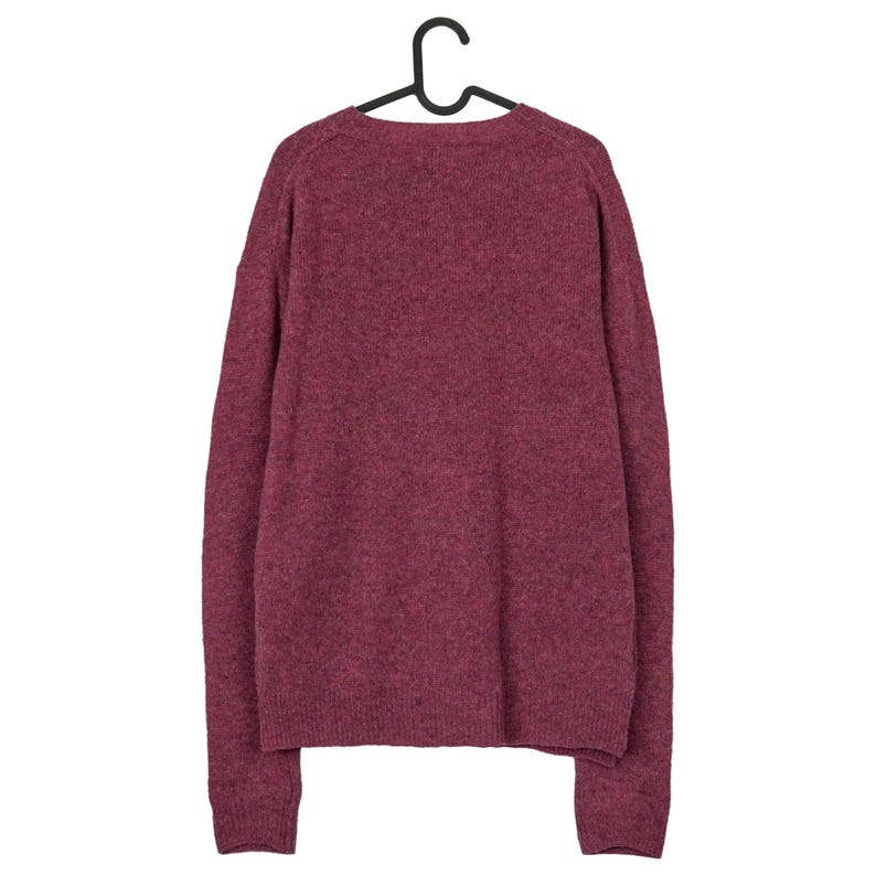 May include: A burgundy-coloured sweater hangs from a black hanger. The sweater has a crew neck and long sleeves. The knit fabric has a textured appearance. The sweater is a solid colour and appears to be made of a soft material.