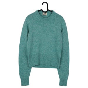 May include: A teal-colored crew neck sweater with long sleeves, hanging on a black hanger. The sweater has a ribbed hem and cuffs. The label reads "Acne Studios".