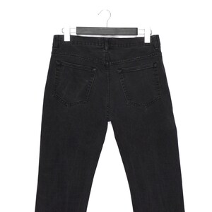 Pu&ograve; includere: Vista posteriore di jeans di denim neri appesi a una gruccia. I jeans hanno due tasche posteriori e un classico design a cinque tasche. Il denim sembra essere di un lavaggio scuro, con dettagli di cucitura visibili. I jeans sono esposti su uno sfondo bianco.