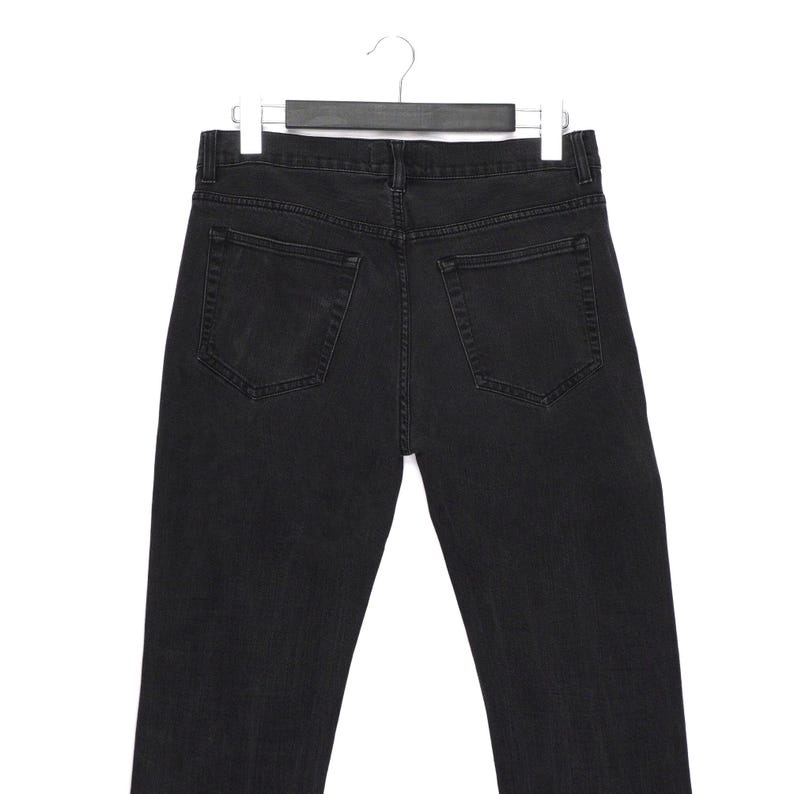 Pu&ograve; includere: Vista posteriore di jeans di denim neri appesi a una gruccia. I jeans hanno due tasche posteriori e un classico design a cinque tasche. Il denim sembra essere di un lavaggio scuro, con dettagli di cucitura visibili. I jeans sono esposti su uno sfondo bianco.