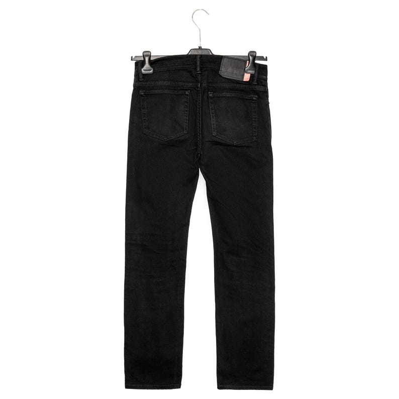 May include: Black denim jeans hanging on a hanger. The jeans have two back pockets and a small leather patch. The jeans are a solid black colour and appear to be new.