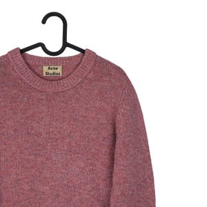 May include: A dusty rose-colored sweater with a crew neck, hanging on a black hanger. The label reads "Acne Studios". The sweater has a textured knit appearance.