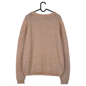 Pu&ograve; includere: Un maglione color beige &egrave; appeso a una gruccia nera. Il maglione ha uno scollo tondo e maniche lunghe. Il materiale appare morbido e soffice. L'indumento &egrave; di un colore neutro, adatto a vari outfit.