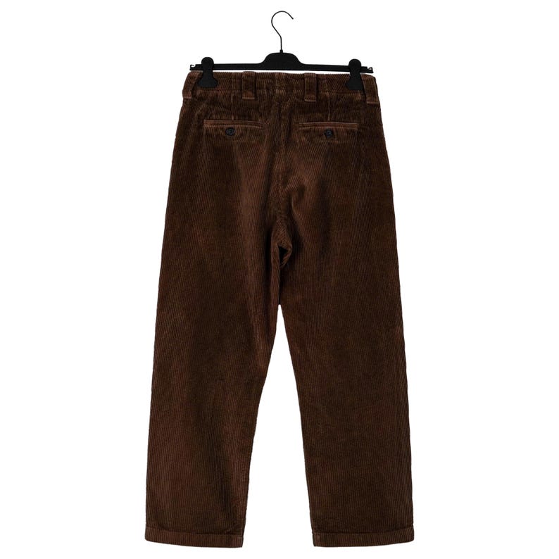 May include: Brown corduroy pants hanging on a black hanger. The pants have a classic design with a button and zipper closure, and two back pockets. The corduroy fabric has a vertical ribbed texture.