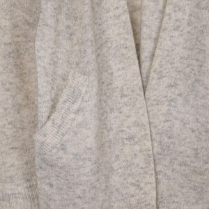 Puede incluir: Primer plano de un c&aacute;rdigan gris claro con un bolsillo. El tejido de punto tiene un patr&oacute;n moteado y un dise&ntilde;o de cuello en V. La tela parece suave y c&oacute;moda, adecuada para superponer.