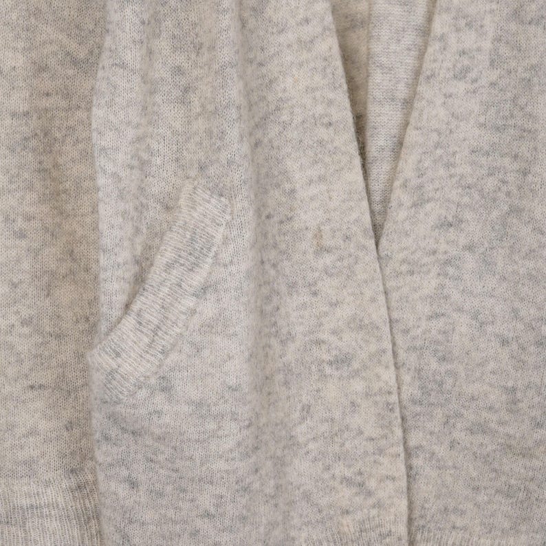 Puede incluir: Primer plano de un c&aacute;rdigan gris claro con un bolsillo. El tejido de punto tiene un patr&oacute;n moteado y un dise&ntilde;o de cuello en V. La tela parece suave y c&oacute;moda, adecuada para superponer.
