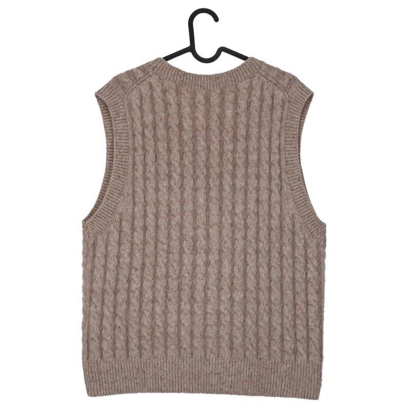 May include: A tan cable-knit sweater vest hangs on a black hanger. The sleeveless garment features a ribbed texture and a rounded neckline. The neutral color and classic design make it a versatile layering piece.