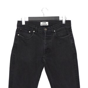 Pu&ograve; includere: Jeans di denim neri appesi a un'appendiabiti. I jeans hanno una chiusura con bottoni, cinque tasche e l'etichetta "ACNE STUDIOS" &egrave; visibile in vita. I jeans sono di un lavaggio scuro e sembrano nuovi.