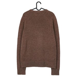 Peut inclure: Un pull marron &agrave; manches longues et col rond, suspendu &agrave; un cintre noir. Le pull a des poignets et un ourlet c&ocirc;tel&eacute;s. Le tissu semble &ecirc;tre un tricot doux et textur&eacute;. V&ecirc;tement d&eacute;contract&eacute;.