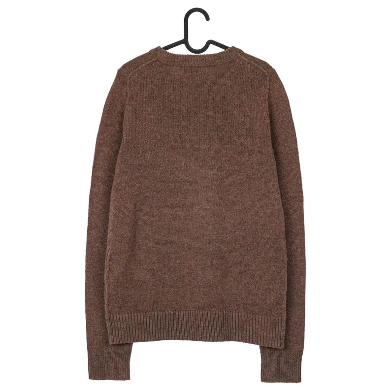 Peut inclure: Un pull marron &agrave; manches longues et col rond, suspendu &agrave; un cintre noir. Le pull a des poignets et un ourlet c&ocirc;tel&eacute;s. Le tissu semble &ecirc;tre un tricot doux et textur&eacute;. V&ecirc;tement d&eacute;contract&eacute;.
