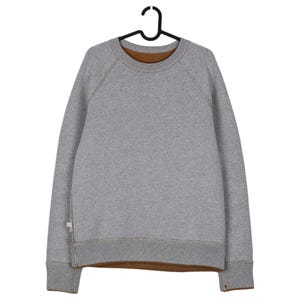May include: A grey sweatshirt with a brown interior and ribbed cuffs and hem. The sweatshirt is hanging on a black hanger. The stitching is a contrasting brown colour.