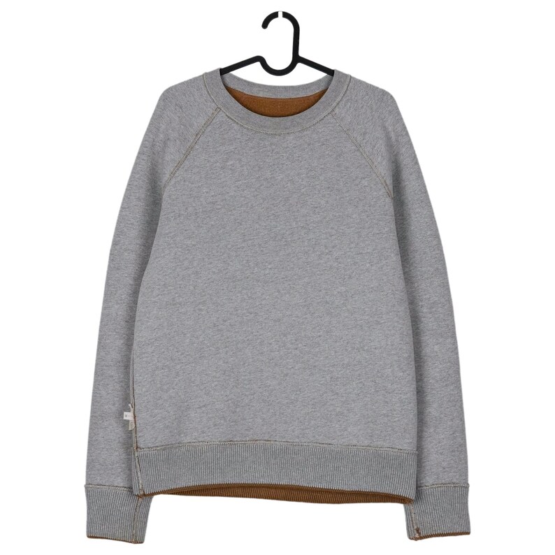 May include: A grey sweatshirt with a brown interior and ribbed cuffs and hem. The sweatshirt is hanging on a black hanger. The stitching is a contrasting brown colour.