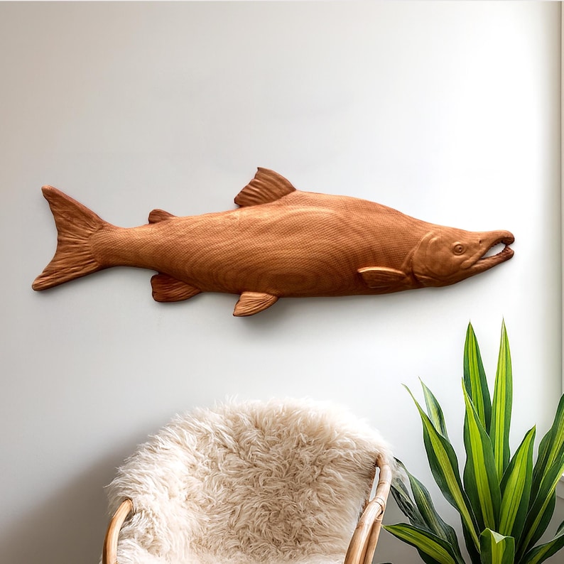 May include: A large, detailed wooden fish sculpture, likely for wall mounting. The fish is carved from light brown wood, with visible grain and texture. It features fins, a tail, and an open mouth, suggesting a salmon or similar species. The sculpture is a decorative item.