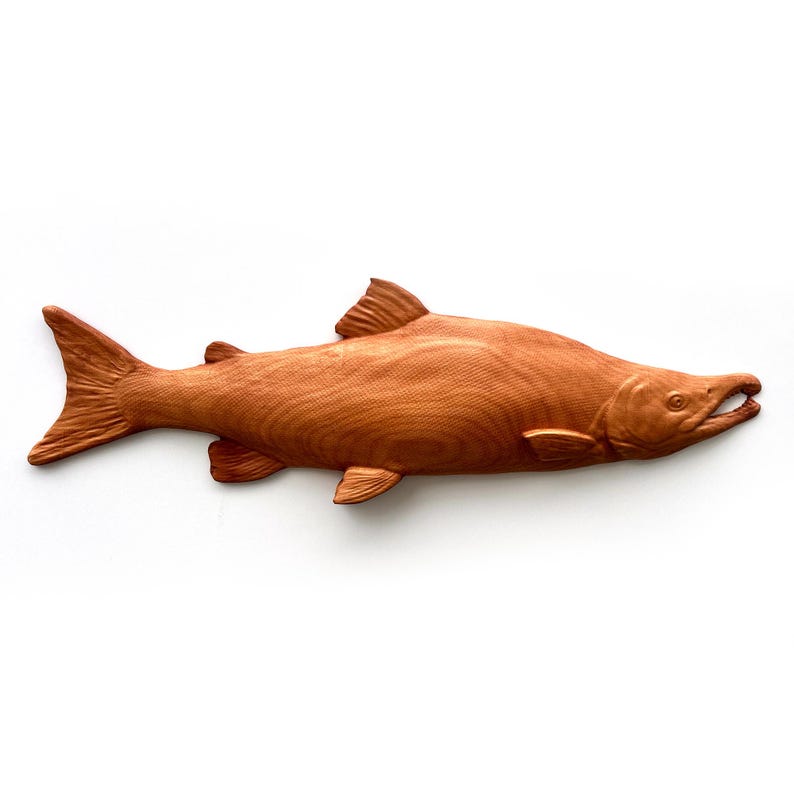 May include: A carved wooden fish sculpture in a natural wood tone. The fish is detailed with fins, a tail, and an open mouth, showcasing the texture of the wood grain. The sculpture is likely for home decor.