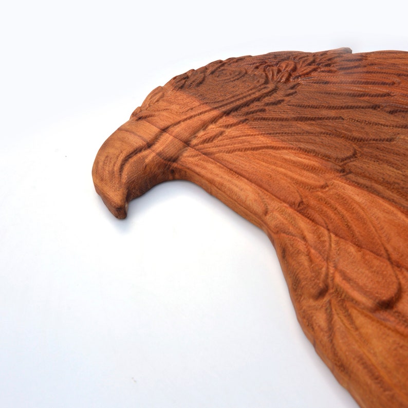 May include: A wooden carving of an eagle's head, with detailed feathers and a reddish-brown colour.