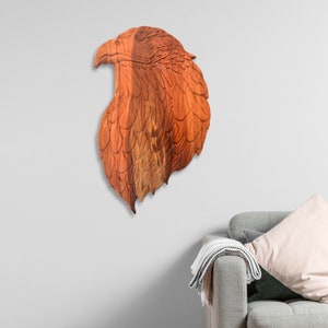 May include: A wooden eagle head sculpture with intricate details, mounted on a white wall. The sculpture is made of reddish-brown wood and has a natural wood grain.