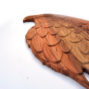 May include: A wooden carving of an eagle wing with detailed feathers. The wing is made of a light brown wood with darker brown accents.