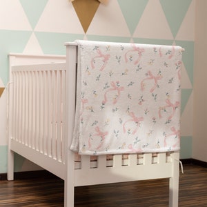 Puede incluir: Cuna blanca con una manta de estampado floral rosa y blanco drapeada sobre el lado. La cuna est&aacute; en una habitaci&oacute;n con una pared de estampado geom&eacute;trico verde claro y blanco.