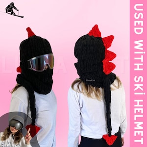May include: Black knitted ski mask with red spikes and a long tail. The mask is worn over a person's head and covers the face. The text "USED WITH SKI HELMET" is visible in the image.