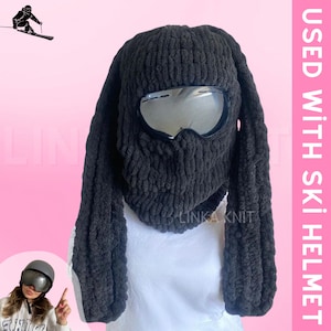 May include: Black knitted ski mask with long ear flaps and a pair of ski goggles. The text "USED WITH SKI HELMET" is written in white on a pink background.